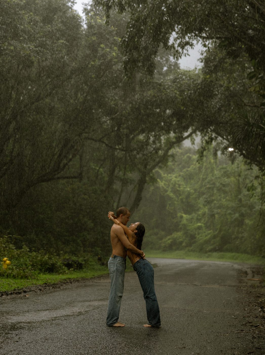 A couple kissing on a wet road beneath tall trees