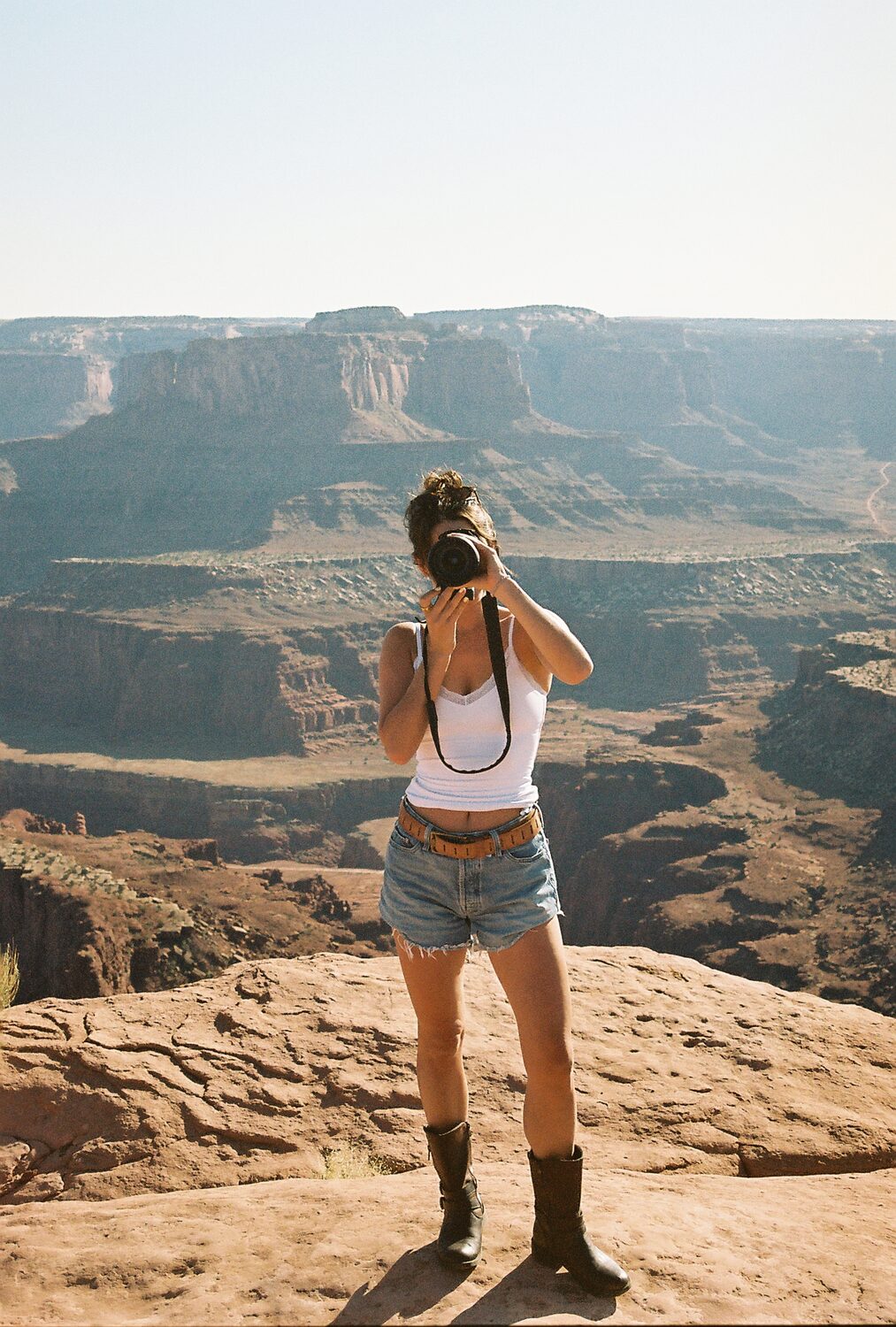 Delani McKee standing at the edge of a red-rock canyon overlook, photographing the view with her film camera