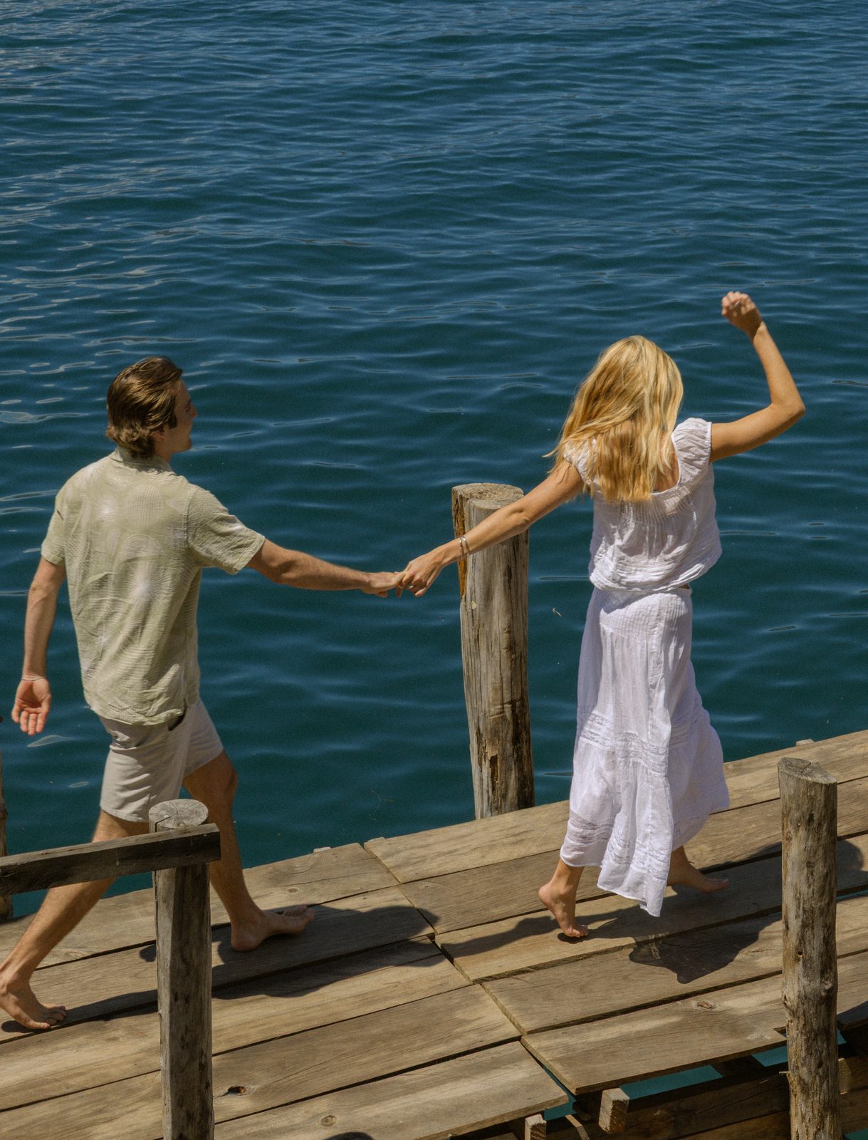 Couple holding hands on a wooden dock over blue water