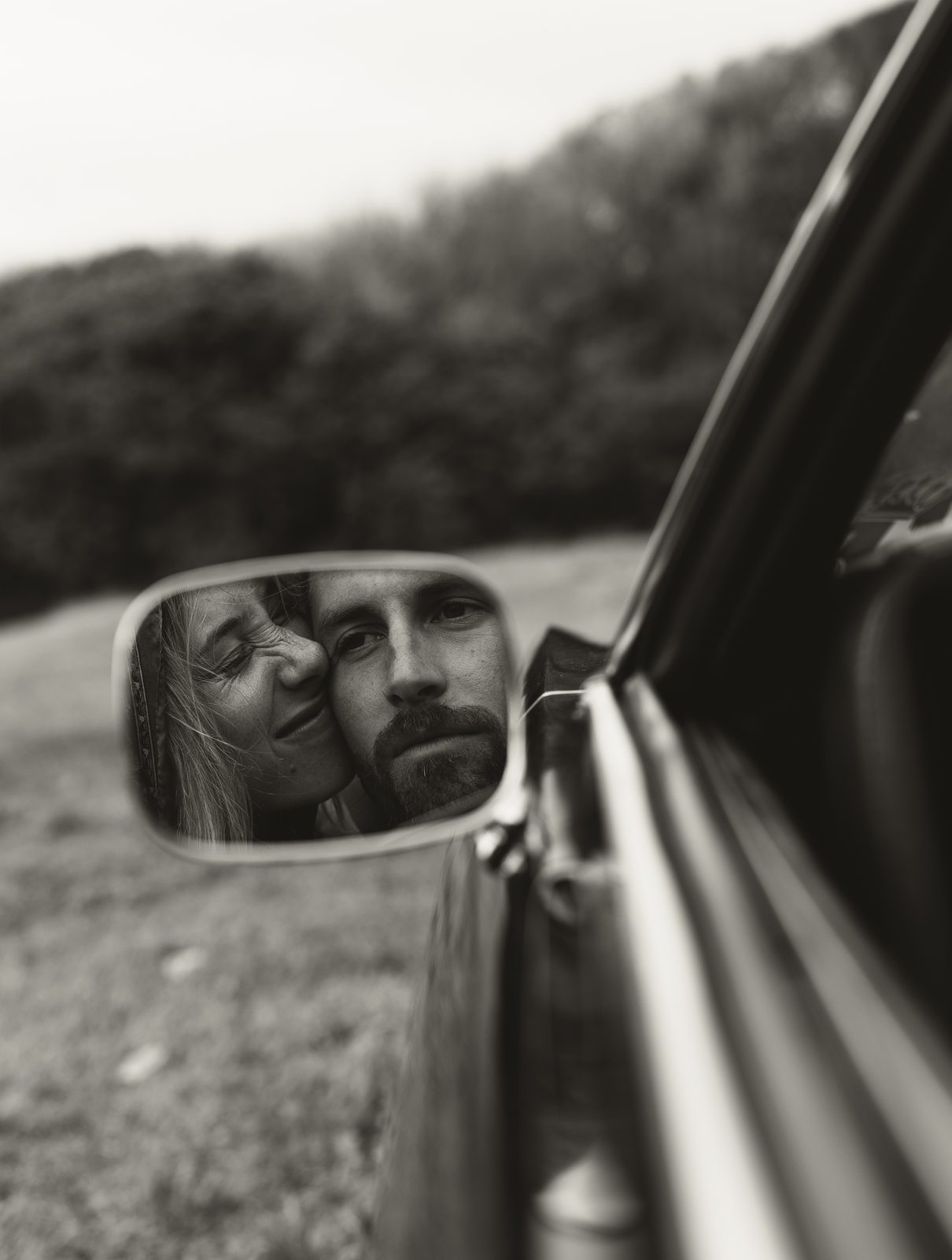 Couple reflected in a vintage car mirror, black and white