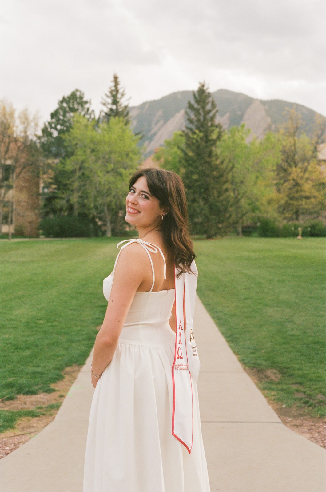 A graduate looking back over her shoulder on a tree-lined path